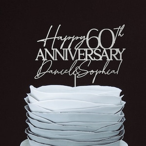 May include: Silver cake topper with the text "Happy 60th Anniversary Daniel & Sophia" on a white cake.