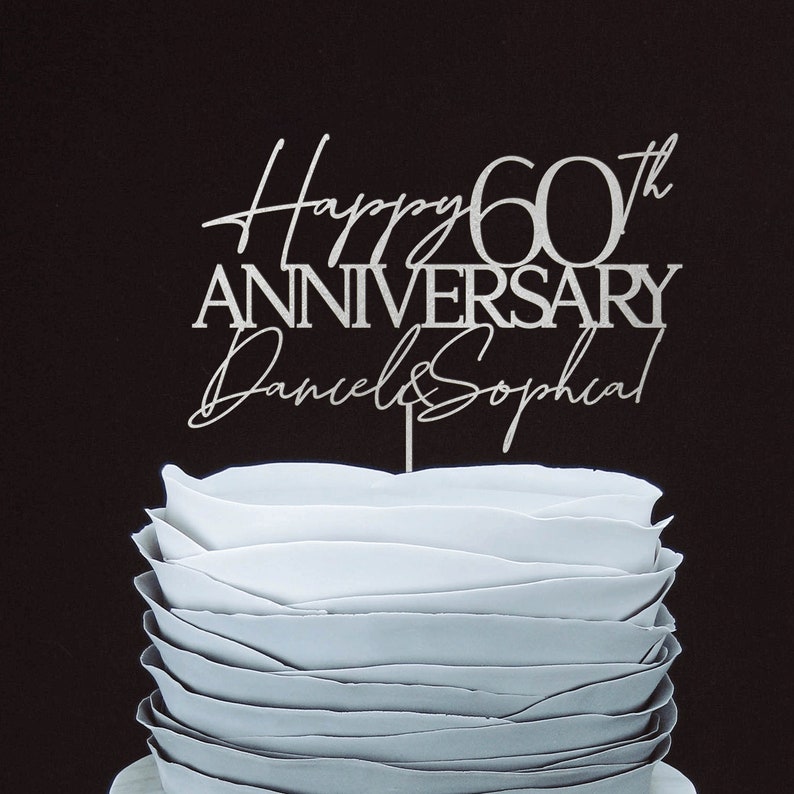 May include: Silver cake topper with the text "Happy 60th Anniversary Daniel & Sophia" on a white cake.