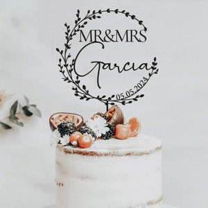 K&ouml;nnte beinhalten: Schwarzer Tortendekor mit einem Kranzdesign und dem Text "MR & MRS Garcia 05.05.2024".