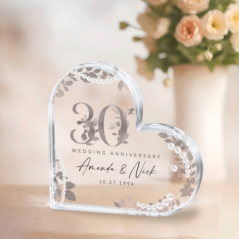 May include: A clear heart-shaped crystal paperweight with a 30th wedding anniversary inscription. The inscription reads "30th Wedding Anniversary Amanda & Nick 10.27.1994". The heart is decorated with a silver floral design and pearl accents.