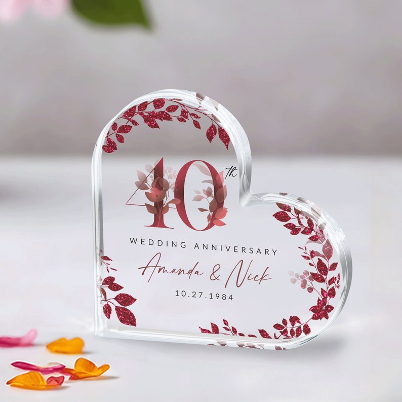 May include: A clear heart-shaped acrylic paperweight with a red and white floral design. The number 40 is in the center with the text "Wedding Anniversary Amanda & Nick 10.27.1984".