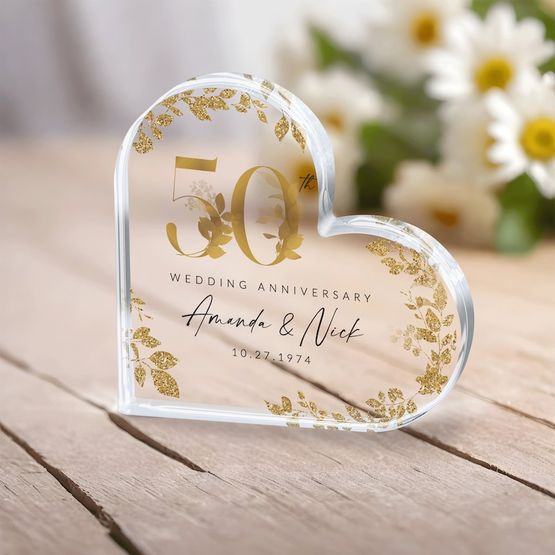 May include: A clear heart-shaped crystal paperweight with gold glitter and floral accents. The number 50 is prominently displayed, along with the text "Wedding Anniversary Amanda & Nick 10.27.1974".