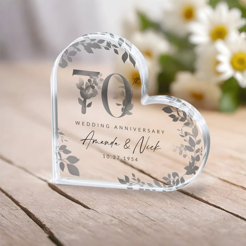 May include: A clear heart-shaped crystal paperweight with a floral design and the text "70th Wedding Anniversary Amanda & Nick 10.27.1954"