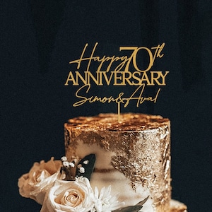 May include: Gold cake topper with the text "Happy 70th Anniversary Simon & Ava" on a gold and white cake with white roses and flowers.