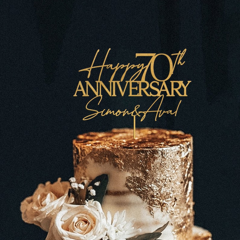 May include: Gold cake topper with the text "Happy 70th Anniversary Simon & Ava" on a gold and white cake with white roses and flowers.