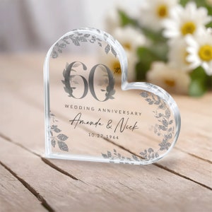 May include: A clear heart-shaped glass paperweight with a silver glitter design. The paperweight features the number 60 with a floral design and the text "Wedding Anniversary Amanda & Nick 10.27.1964".