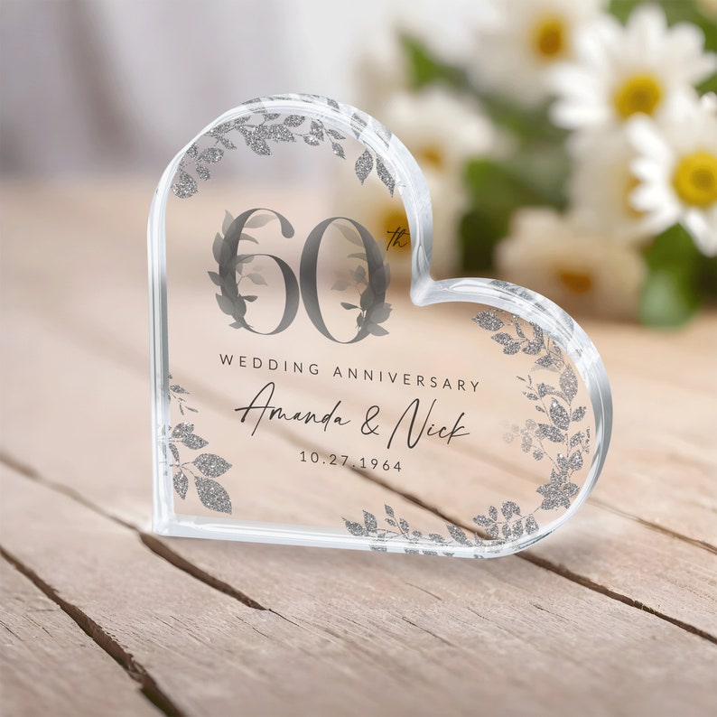 May include: A clear heart-shaped glass paperweight with a silver glitter design. The paperweight features the number 60 with a floral design and the text "Wedding Anniversary Amanda & Nick 10.27.1964".