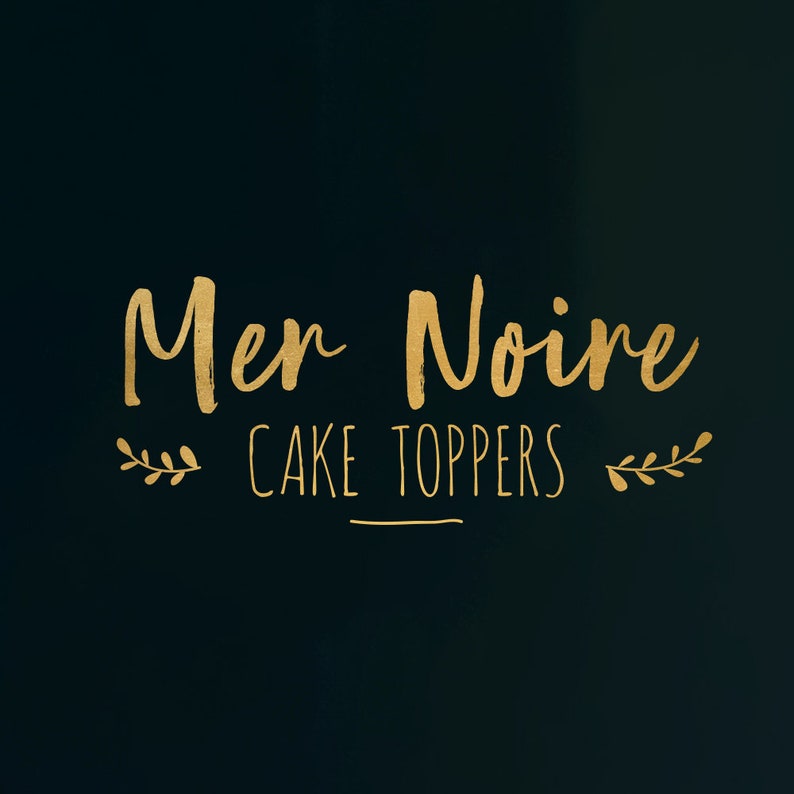 Puede incluir: Letras doradas sobre fondo negro que dicen "Mer Noire Cake Toppers" con un peque&ntilde;o dise&ntilde;o de hojas a cada lado del texto.