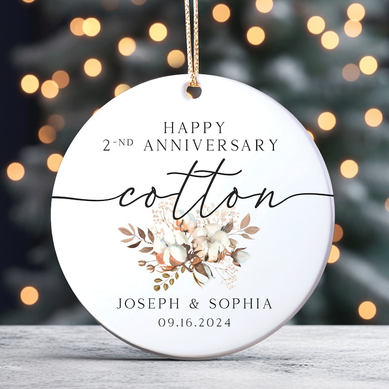 Peut inclure: Une boule ronde blanche avec le texte "Happy 2-nd Anniversary Cotton" en &eacute;criture cursive noire. Une illustration aquarelle d'une boule de coton avec des feuilles brunes se trouve sous le texte. Les noms "Joseph & Sophia" et la date "09.16.2024" sont imprim&eacute;s sous l'illustration.