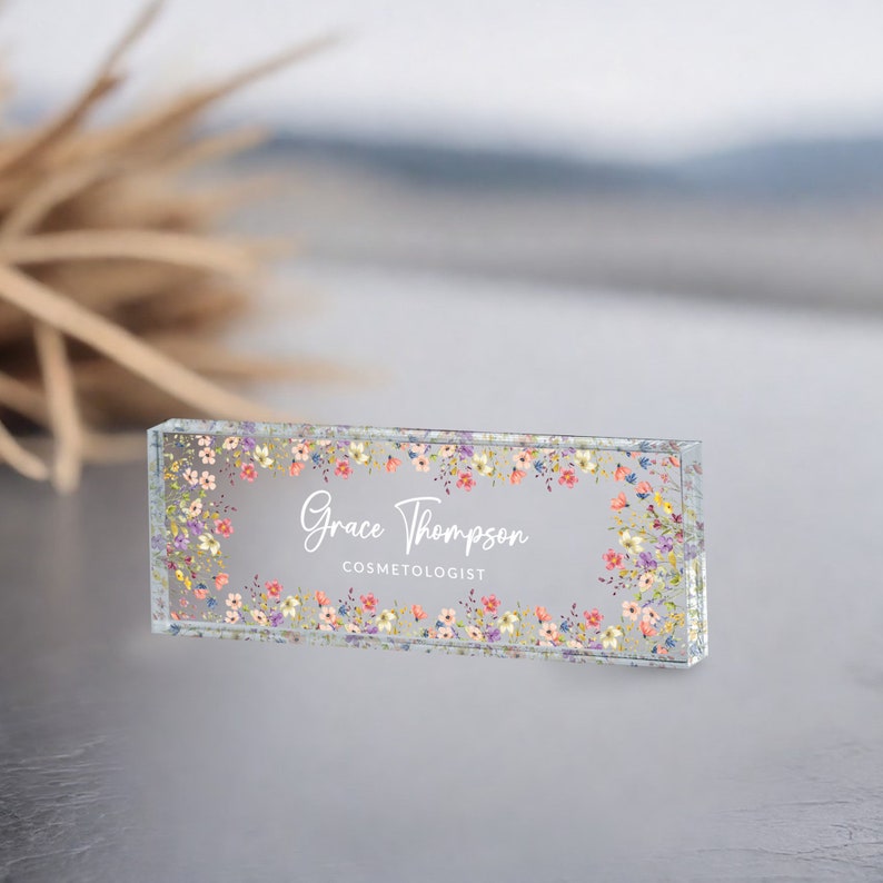 May include: A clear glass desk nameplate with a floral border and the text "Grace Thompson COSMETOLOGIST".