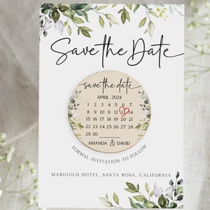 Puede incluir: Tarjeta de guardar la fecha con un calendario circular de madera que presenta un coraz&oacute;n rojo el 13 de abril. La tarjeta est&aacute; decorada con ilustraciones florales de acuarela verde y blanca. El texto dice "Save the Date" y "Amanda & David" con la ubicaci&oacute;n "Marigold Hotel, Santa Rosa, California".