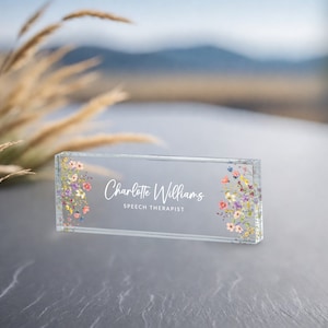 May include: A clear glass desk nameplate with a floral design and the text "Charlotte Williams, Speech Therapist".