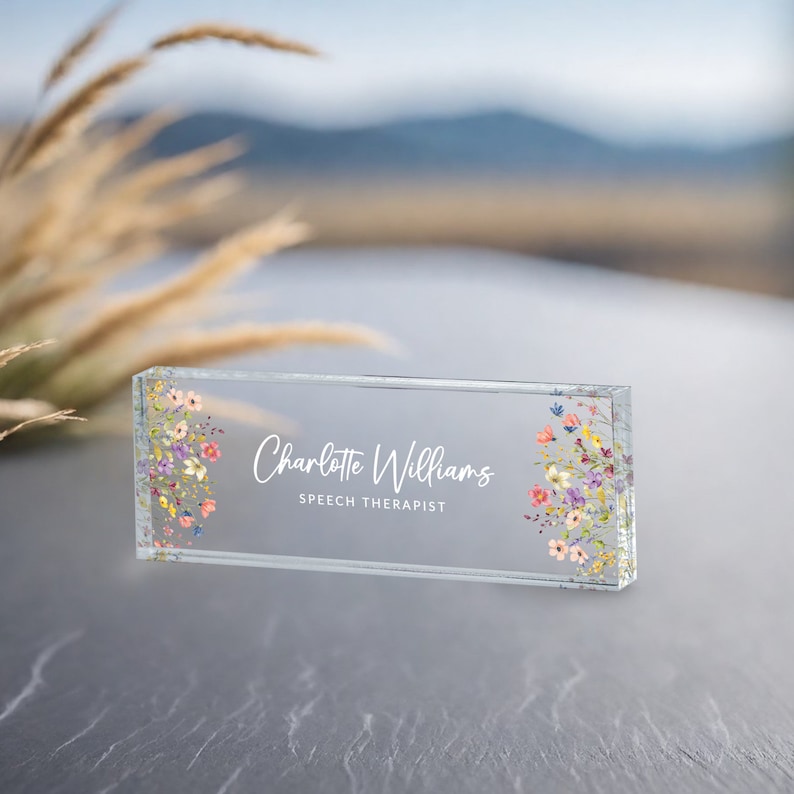 May include: A clear glass desk nameplate with a floral design and the text "Charlotte Williams, Speech Therapist".