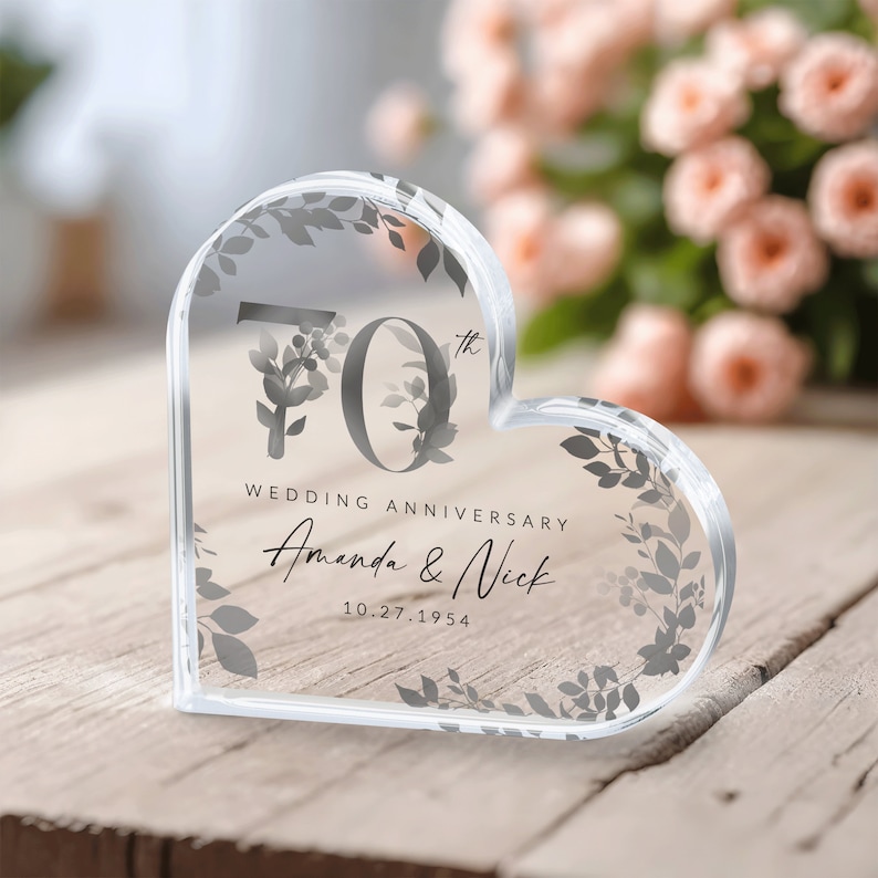 May include: A clear heart-shaped crystal paperweight with a floral design and the text "70th Wedding Anniversary Amanda & Nick 10.27.1954"