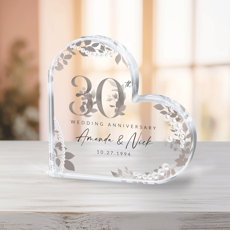 May include: A clear heart-shaped glass paperweight with a 30th wedding anniversary inscription. The inscription reads "30th Wedding Anniversary Amanda & Nick 10.27.1994".