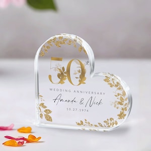 May include: A clear heart-shaped acrylic paperweight with gold glitter accents and a gold inscription that reads "50th Wedding Anniversary Amanda & Nick 10.27.1974".