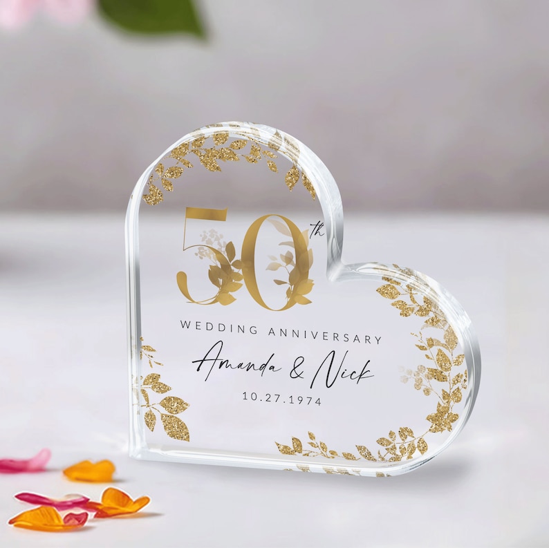May include: A clear heart-shaped acrylic paperweight with gold glitter accents and a gold inscription that reads "50th Wedding Anniversary Amanda & Nick 10.27.1974".