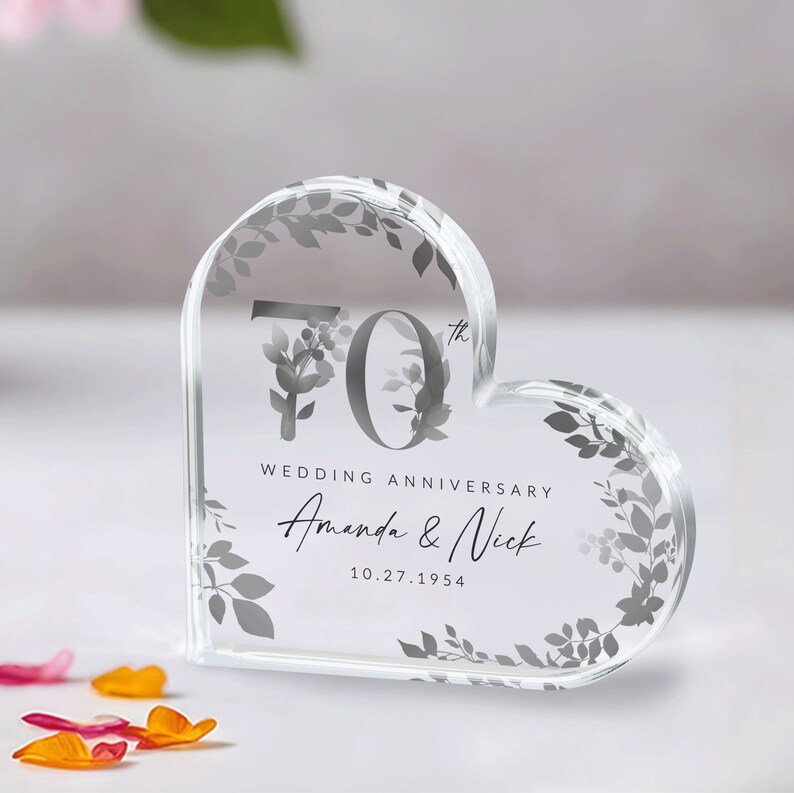 May include: A clear heart-shaped crystal paperweight with a floral design and the text "70th Wedding Anniversary Amanda & Nick 10.27.1954"