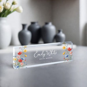 May include: A clear acrylic desk nameplate with a floral design and the text "Emily White Social Worker".