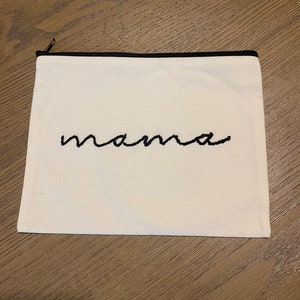 May include: A white canvas zippered pouch with a black zipper and black embroidered text that says "mama".