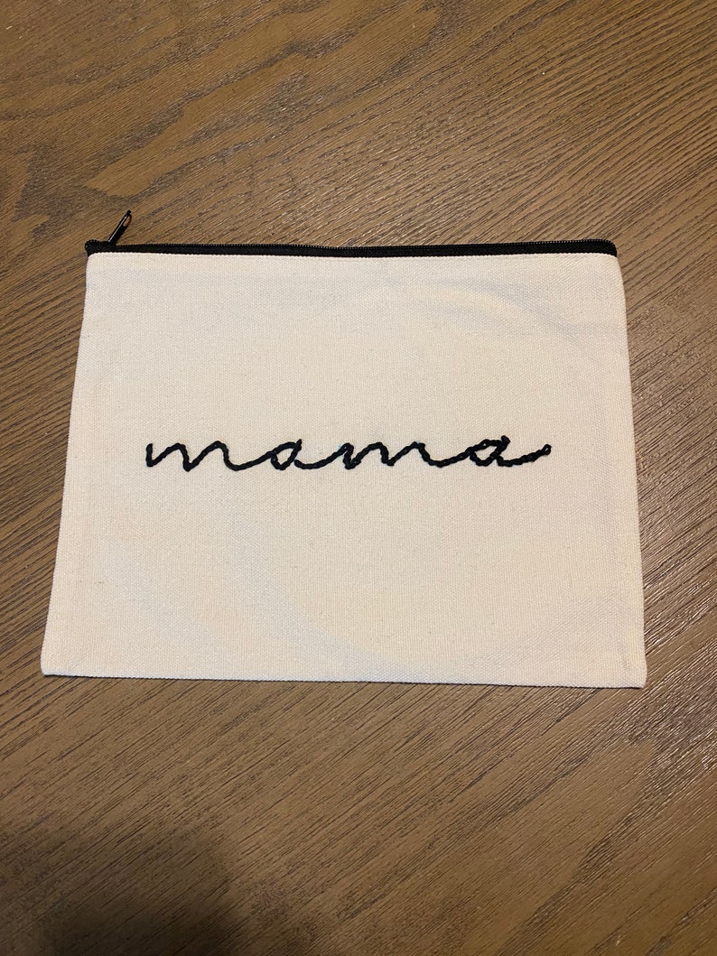 May include: A white canvas zippered pouch with a black zipper and black embroidered text that says "mama".