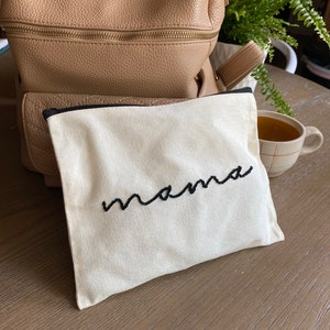 May include: A white canvas pouch with a black zipper and the word "mama" embroidered in black thread.