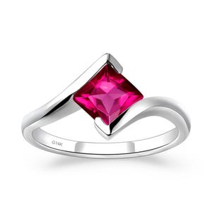 May include: A silver ring with a vibrant, square-cut, magenta gemstone. The ring band curves gracefully, with the gemstone set in a diagonal, modern design. The inscription "G14K" is visible on the band. A piece of jewelry.
