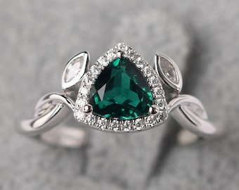 May include: A silver ring featuring a triangular, emerald-green gemstone surrounded by a halo of small, clear stones. The ring has a twisted band design with leaf-shaped accents on either side of the central stone.