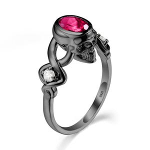 May include: A black skull ring with a ruby-colored oval gemstone and two smaller white gemstones. The ring has a twisted design and is marked with "S925".