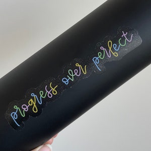 May include: Black water bottle with a rainbow colored sticker that says "progress over perfect"