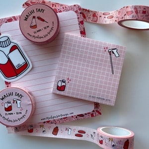 May include: A collection of pink stationery items, including washi tape rolls, sticky notes, and a sticker. The washi tape is 15 mm wide and 10 m long, featuring a repeating pattern of lab equipment. The sticker and sticky notes have illustrations of lab bottles.