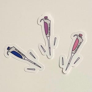 May include: Three stickers of laboratory pipettes in blue, pink, and purple. Each pipette has a different color scheme and is outlined in white. The stickers are on a white background.