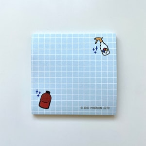May include: Square light blue notepad with a grid pattern. The notepad features cartoon illustrations of a brown bottle and a spray bottle with a colorful label. The text "© 2022 MADISON SETO" is printed on the bottom right corner.