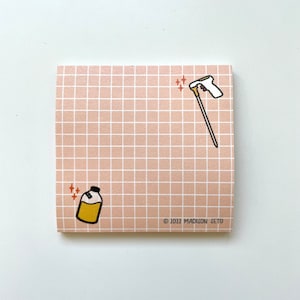 May include: A square notepad with a grid pattern in light brown. The notepad features illustrations of a bottle with yellow liquid and a cleaning tool. The text "© 2022 MADISON SETO" is printed on the bottom right corner.