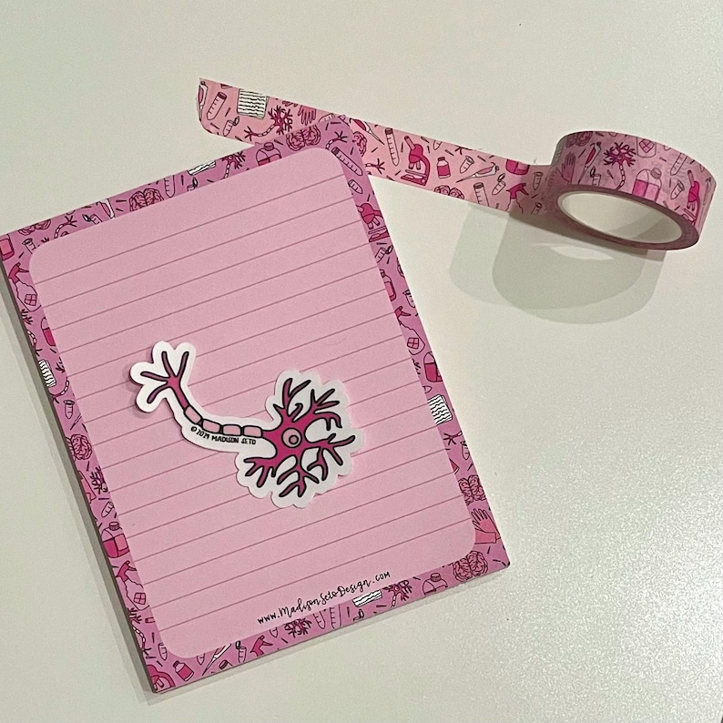 May include: A pink notepad with lined pages and a neuron sticker, alongside a roll of pink decorative tape. The tape and the notepad's border feature a repeating pattern of science-themed illustrations.