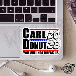 May include: A white sticker on a laptop with the words "CARL 20 DONUT 28 YOU WILL NOT BREAK US" in black and red. The word "DONUT" is above a blue bar with white stars. The laptop keyboard is visible.