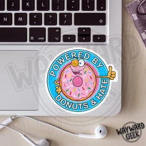 May include: A circular sticker featuring a cartoon donut with pink frosting and colorful sprinkles. The donut has arms, a face, and is giving a thumbs up. The blue border contains the text POWERED BY DONUTS & HATE in bold black letters.