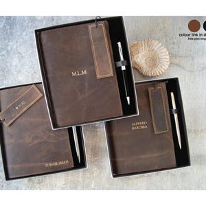 Puede incluir: Tres diarios de cuero marrón oscuro presentados en cajas de regalo negras. Cada diario incluye un marcapáginas de cuero a juego y un bolígrafo de metal. Las portadas están personalizadas con grabados M.L.M, YOU, ZUBAIR SHAH y ALFREDO BAROSSA.