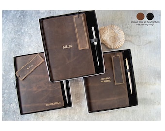 Könnte beinhalten: Drei dunkelbraune Leder-Notizbücher in schwarzen Geschenkboxen. Jedes Notizbuch enthält ein passendes Leder-Lesezeichen und einen Metallstift. Die Einbände sind mit den Gravuren M.L.M, YOU, ZUBAIR SHAH und ALFREDO BAROSSA personalisiert.