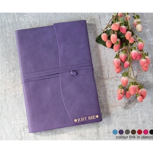 May include: Purple leather journal with a gold heart and the text "JUST BEE" embossed on the cover. The journal has a leather strap closure and is tied with a knot.