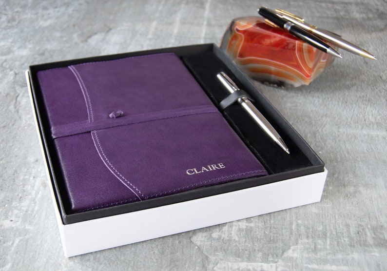 May include: A purple leather journal with the name "CLAIRE" embossed on the cover, a silver pen, and a red agate paperweight in a white gift box.
