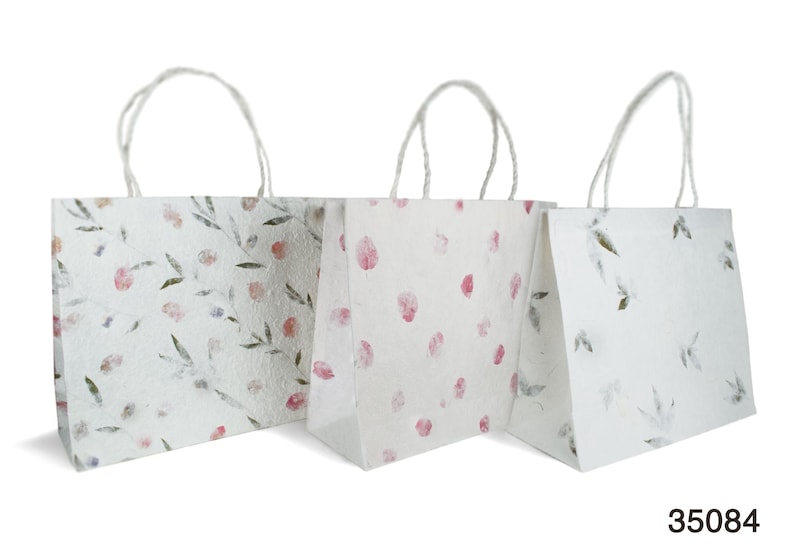 K&ouml;nnte beinhalten: Drei wei&szlig;e Papiert&uuml;ten mit Blumenmustern. Die Taschen haben wei&szlig;e Henkel und sind mit rosa und gr&uuml;nen Blumendesigns verziert.