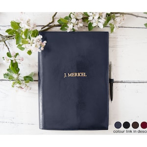 May include: A navy blue leather bound journal with gold lettering that reads "J. MERKEL". A silver pen is tucked into the journal's binding.