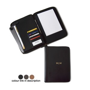 May include: Black leather zipped portfolio with a notepad, card slots, and a phone pocket. The portfolio is open and the inside is visible. The portfolio has the initials "M.J.M." embossed in gold on the front.