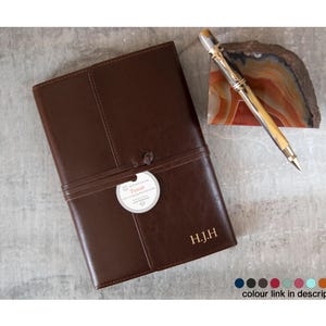 Puede incluir: Un diario de cuero marr&oacute;n con un monograma dorado en relieve "H.J.H." y una etiqueta blanca con la palabra "Truth" en ella. El diario est&aacute; atado con una correa de cuero marr&oacute;n.