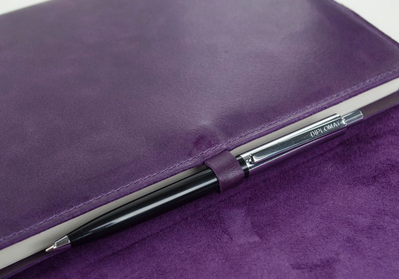 May include: A purple leather notebook with a silver pen inside. The pen has the word "DIPLOMAT" printed on it.