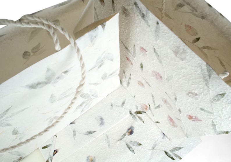 K&ouml;nnte beinhalten: Drei wei&szlig;e Papier-Geschenkbeutel mit Blumenmuster und einem Seilhenkel. Die Beutel sind aus recyceltem Papier mit eingebetteten Blumen und Bl&auml;ttern.