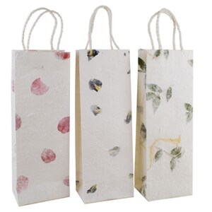 K&ouml;nnte beinhalten: Drei wei&szlig;e Papiert&uuml;ten mit Henkeln. Die Taschen haben verschiedene Blumenmuster: rosa Bl&uuml;tenbl&auml;tter, blaue und gelbe Blumen und gr&uuml;ne Bl&auml;tter.