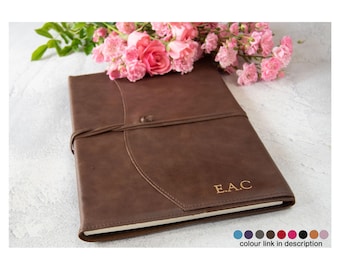 Könnte beinhalten: Ein braunes, ledergebundenes Tagebuch mit einer goldenen Prägung "E.A.C." und einem Verschluss mit einer Schnur. Das Tagebuch liegt auf einer weißen Oberfläche mit rosa Blumen.