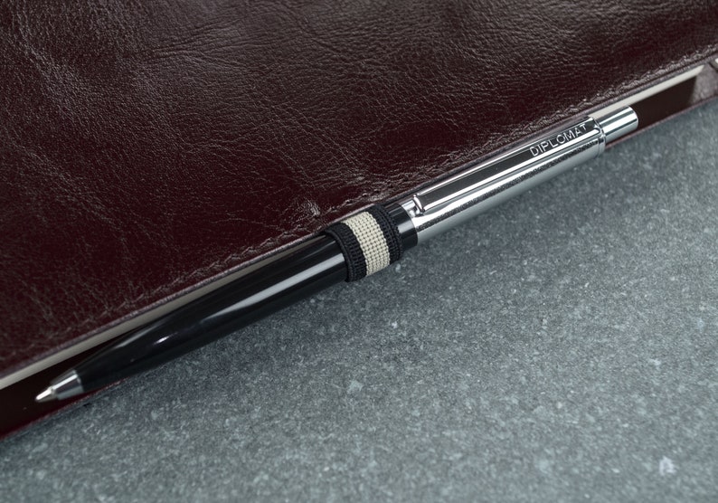 Puede incluir: Un bol&iacute;grafo plateado con un cuerpo negro y una banda blanca y negra. El bol&iacute;grafo est&aacute; grabado con la palabra "Diplomat".